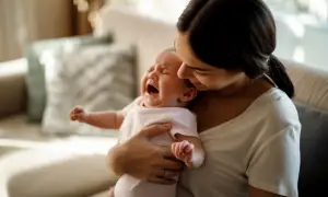 En mamma tröstar sitt kolikbarn som gråter intensivt i hennes famn.