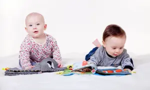 Två bebisar utforskar tygböcker. Den ena sitter och tittar framåt, den andra ligger på mage och bläddrar. Ett litet språng 7 mot nya upptäckter.
