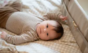 En 1 månads bebis sover inte, utan ligger vaken och tittar med sina stora ögon. Bebisen har en randig tröja och ligger på en rutig filt.