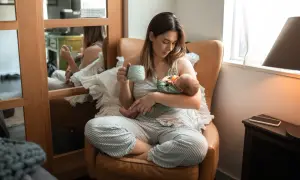 En mamma med en bebis i famnen, hon håller en mugg. En lugn stund med choklad amning.