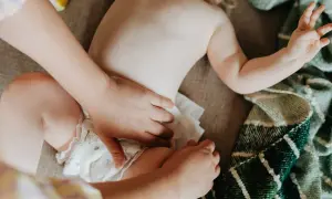 En bebis mage och blöja, någon torkar bort slemmigt bajs.