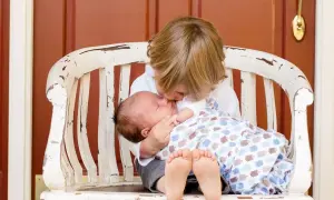 Äldre syskonet kysser sin nyfödda bebis på en sliten bänk. En vacker stund att få syskon.