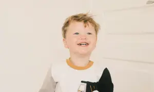 Glad pojke med blont hår och blå ögon ler mot kameran. Han har på sig en tröja med en lastbil på. Han är det andra barnet i familjen.