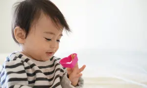 En 14 månaders bebis med randig tröja leker med en rosa hjärtformad leksak.