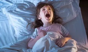 Ett litet barn vaknar och skriker hysteriskt i sängen, med öppen mun och uppspärrade ögon.