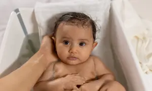 Söt bebis i badet, med lite skorv i håret. En hand tvättar försiktigt.