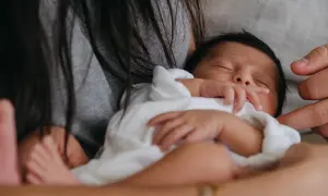 En bebis sover tryggt i famnen, insvept i vitt. En hand vilar mjukt på barnets huvud. En lugn stund för natta bebis.