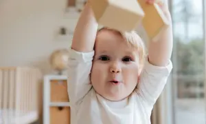 En bebis med stora ögon håller upp träklossar, nyfiken på världen. Man undrar hur långt ser en bebis när den utforskar sin omgivning.