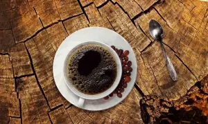 En kopp kaffe med bönor och en sked på en trädstam. För den som ammar kan koffein vara en känslig fråga.