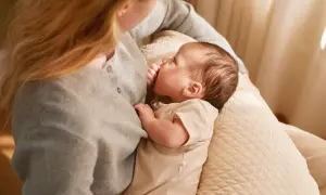 En mamma ammar sin bebis, som är cirka 6 veckor gammal. Mjukt ljus faller in från sidan.