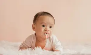 Söt bebis med mjölk runt munnen, kanske lite reflux bebis. Ligger på en fluffig matta.