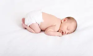 En sovande bebis i blöja, drömmer sött. Kanske undrar du hur mycket sover en 3 månaders bebis? Denna lilla sover djupt.