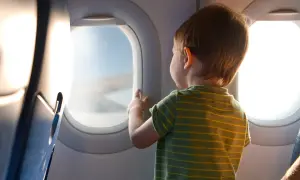 Liten pojke med randig tröja tittar ut genom flygplansfönstret. En magisk upplevelse att flyga med barn.