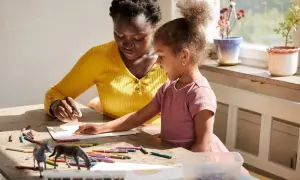 Ensamstående mamma och dotter pysslar vid ett bord med kritor och leksaker.