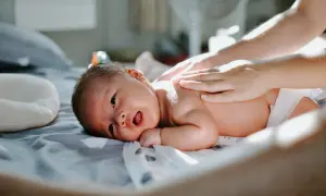 En bebis 2 månader får massage på ryggen. Solen lyser på den lilla kroppen.