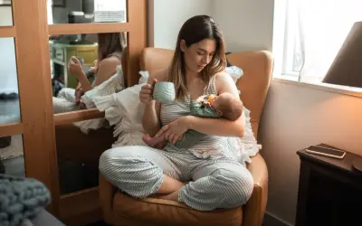 En mamma med en bebis i famnen, hon håller en mugg. En lugn stund med choklad amning.
