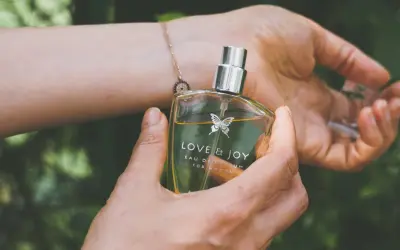 En hand håller en parfymflaska med texten "LOVE & JOY". Doften kan vara en fin present till en parfym gravid.