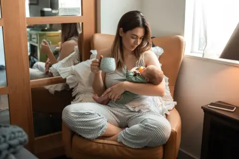 En mamma med en bebis i famnen, hon håller en mugg. En lugn stund med choklad amning.