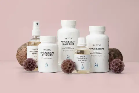 Flera flaskor och burkar med magnesiumtillskott, inklusive magnesium tillskott gravid, står uppradade med stenar och torkade blommor.