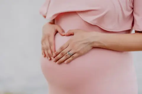 Gravid mage i vecka 21, en hand formar ett hjärta på magen.