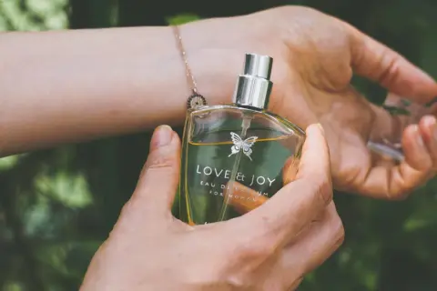 En hand håller en parfymflaska med texten "LOVE & JOY". Doften kan vara en fin present till en parfym gravid.