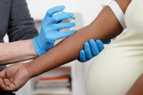 Blodprov tas för nipt test vecka 10. En hand med blå handske håller armen medan en annan hand med blå handske för in en nål.