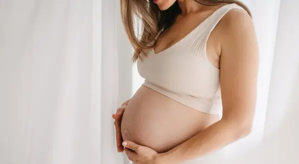 Gravid kvinna med händer på magen, mjukt ljus. Hon kanske använder bio oil gravid för att ta hand om sin hud.