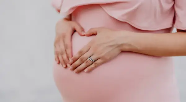 Gravid mage i vecka 21, en hand formar ett hjärta på magen.