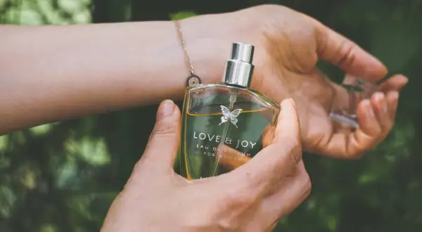 En hand håller en parfymflaska med texten "LOVE & JOY". Doften kan vara en fin present till en parfym gravid.