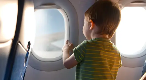 Liten pojke med randig tröja tittar ut genom flygplansfönstret. En magisk upplevelse att flyga med barn.