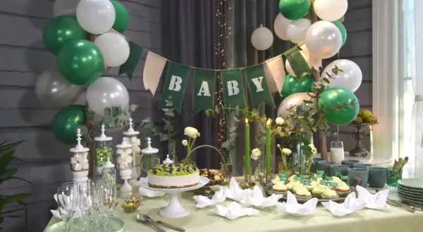 Grön och vit baby shower-dekoration med ballonger, en "BABY"-banderoll, tårta, cupcakes och godis.