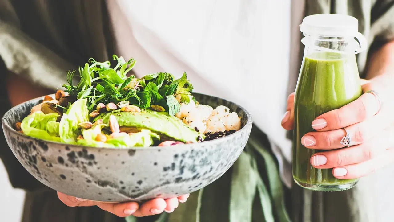 En person håller en skål med en hälsosam sallad och en grön smoothie. Perfekt bra mat gravid för näring och energi.