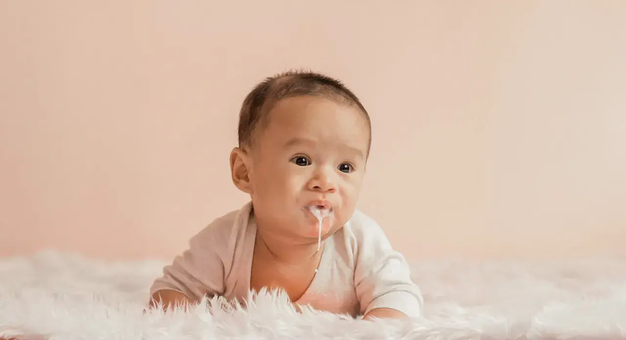 Söt bebis med mjölk runt munnen, kanske lite reflux bebis. Ligger på en fluffig matta.