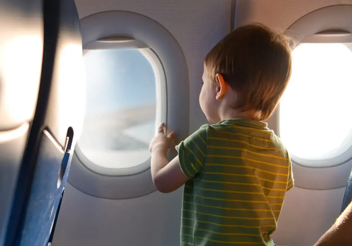 Liten pojke med randig tröja tittar ut genom flygplansfönstret. En magisk upplevelse att flyga med barn.