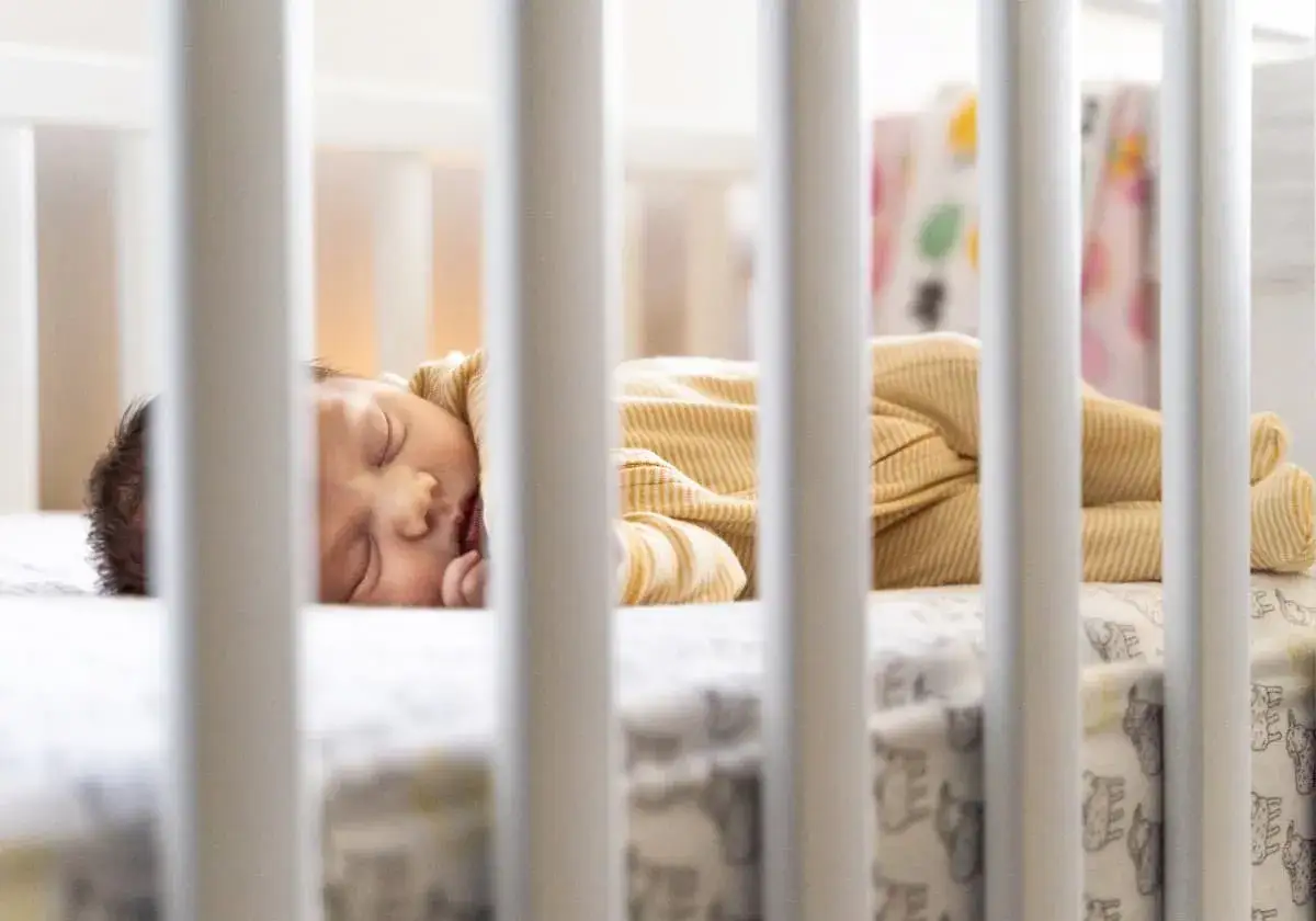 Sover sött i spjälsängen, en liten bebis i gulrandig pyjamas. Kanske en 4 månaders regression som gör att den lilla behöver extra trygghet.