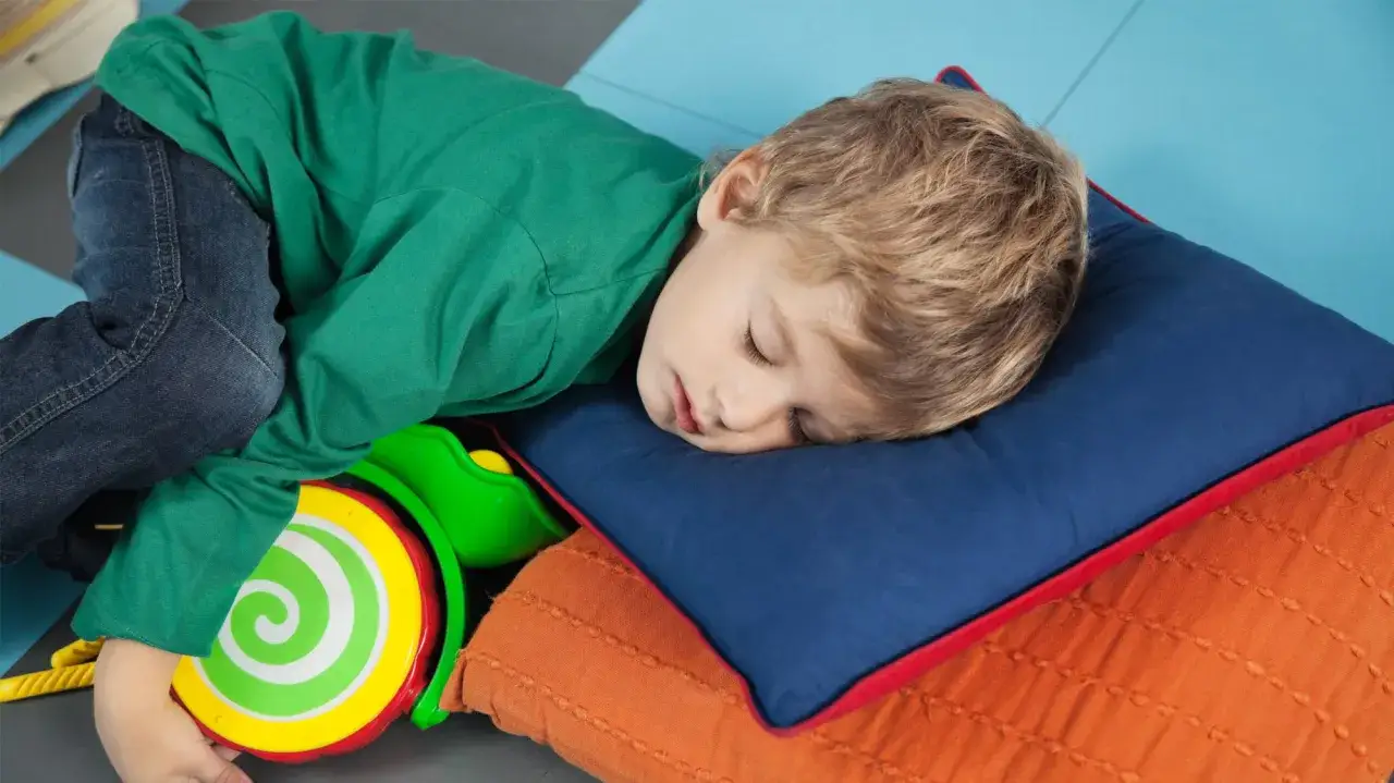 Liten pojke sover på kuddar med en leksak. Dagsömnen är över, nu är det dags att leka!