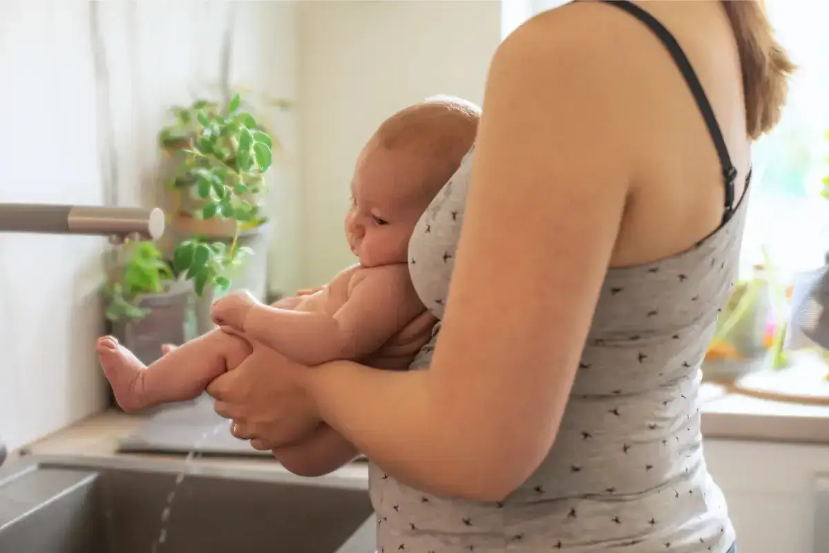 En person håller en bebis över ett handfat. Vatten rinner från kranen. En fin stund av baby potting.