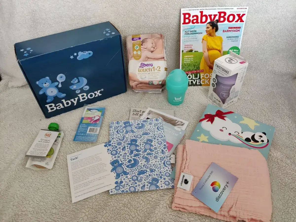 BabyBox från Kronans Apotek med blöjor, tidning, nappflaska, barnmat och en mjuk filt.