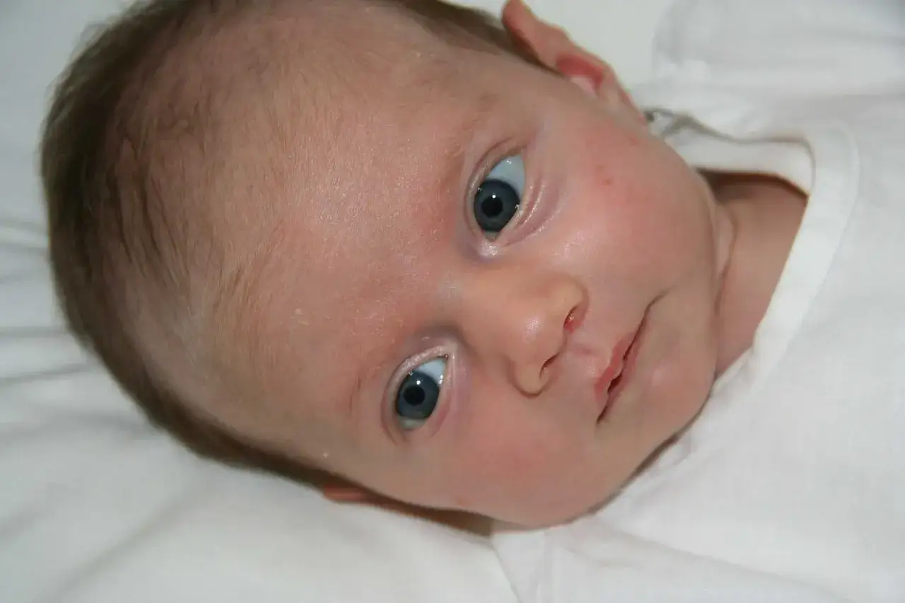En n&auml;rbild p&aring; en bebis med bl&aring; &ouml;gon och lite babyakne p&aring; kinderna.