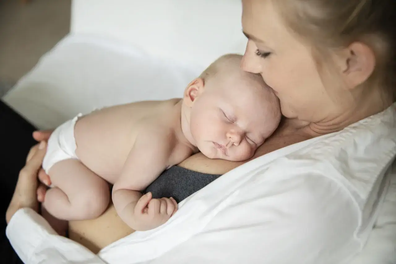 En mamma h&aring;ller sitt sovande sp&auml;dbarn t&auml;tt intill sig. Barnet sover lugnt, kanske efter att ha ammat var tredje timme.