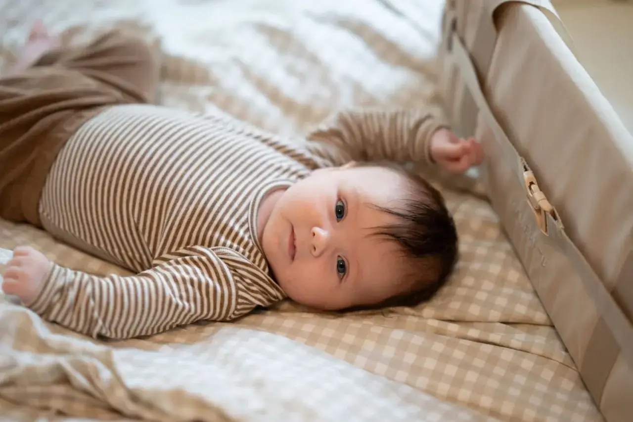 En bebis i randig body ligger på en rutig filt. Undrar du hur mycket sover en 3 månaders bebis?