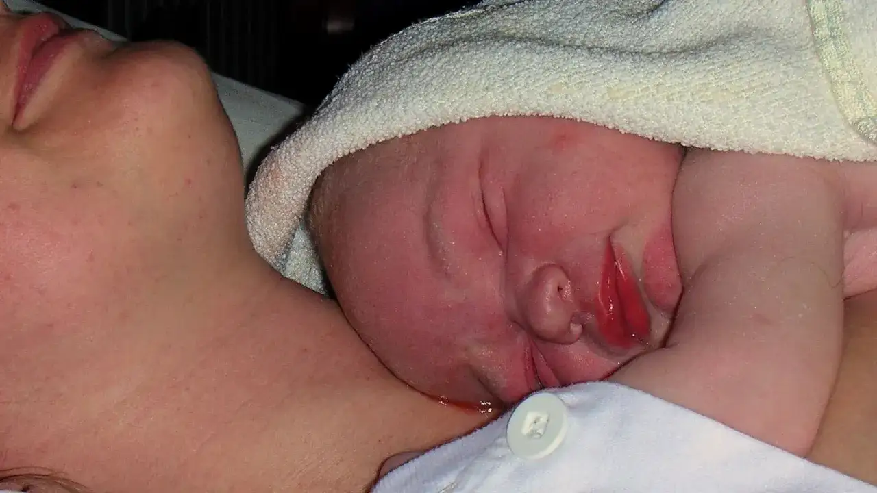 Nära hud mot hud, en nyfödd bebis vilar mot sin mammas hals, insvept i en mjuk handduk.