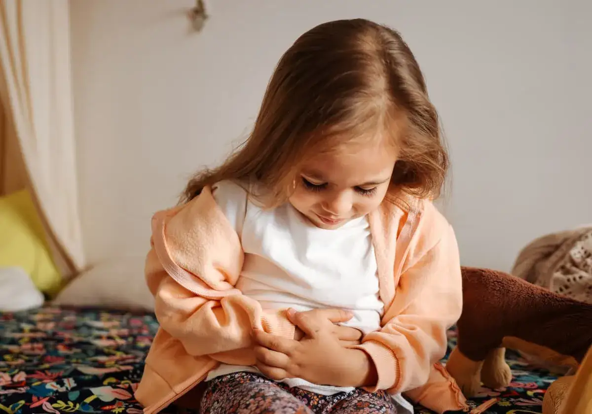 Liten flicka med h&auml;nderna p&aring; magen, ser orolig ut. Kanske b&ouml;rjar magsjuka inkubationstid ge sig till k&auml;nna.