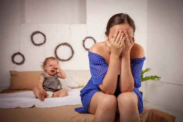En mamma gömmer ansiktet i händerna medan hennes bebis gråter. Kanske en tuff period med 4 månaders regression.