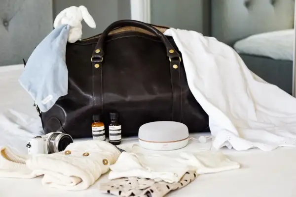 Packlista bb: mörk väska, bebiskläder, nalle, kamera, högtalare och två små flaskor.