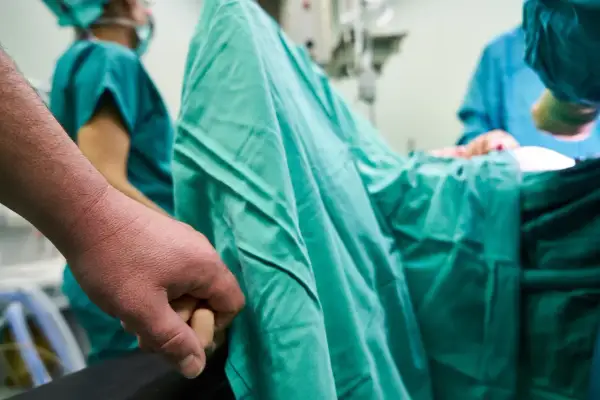 En partner till gravid håller handen under en operation.