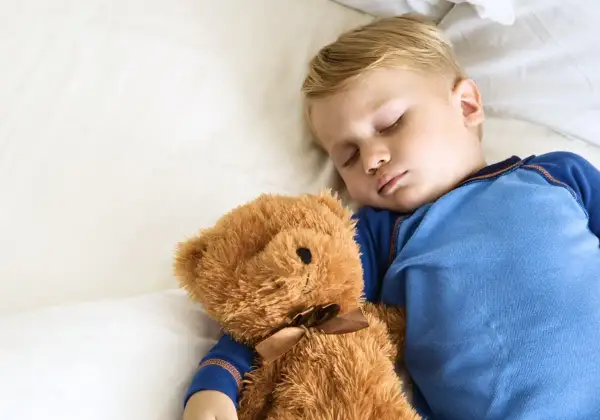 En liten pojke sover sött med sin nallebjörn. Kanske är det dags att sluta sova på dagen och vara vaken istället.