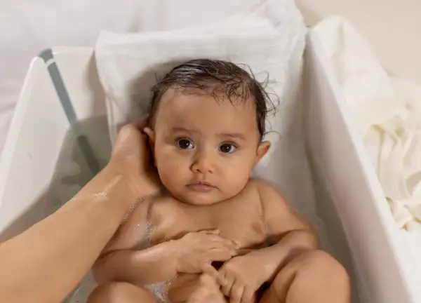 Söt bebis i badet, med lite skorv i håret. En hand tvättar försiktigt.