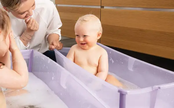 Glad bebis i badbalja, en mamma tittar på. Frågan "hur ofta bada bebis" kan besvaras med att det är mysigt att bada ofta!