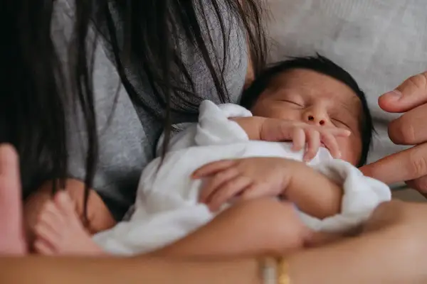 En bebis sover tryggt i famnen, insvept i vitt. En hand vilar mjukt på barnets huvud. En lugn stund för natta bebis.